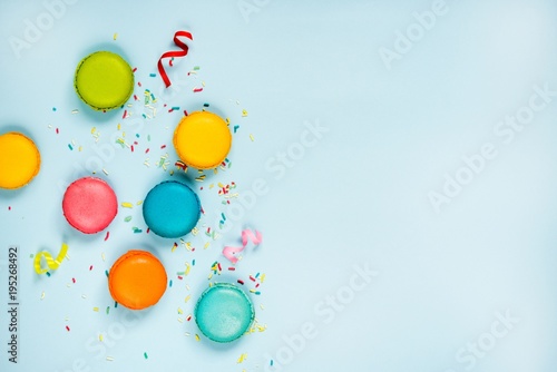 Top view of colorful macaroons, sugar sprinkles and party ribbons arranged over blue background. Copy space.