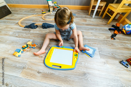A three year old girl playing with magnetic  drawing board on the floor in her room