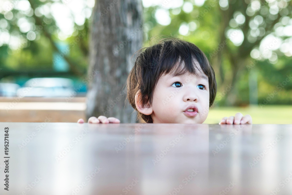 Closeup asian kid comes out from the table in the garden background with copy space Closeup asian kid comes out from the table in the garden background with copy space