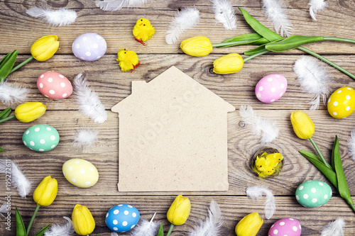 Home symbol with Easter eggs, chickens and yellow tulips on old wooden background. Space for text.