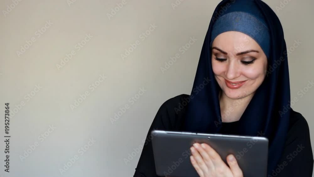 Portrait of a beautiful Arab woman who smiles and looks at the screen of a tablet and dials a message, communicates on the Internet and social networks, using a Tablet PC. Lifestyle and leisure of Portrait of a beautiful Arab woman who smiles and looks at the screen of a tablet and dials a message, communicates on the Internet and social networks, using a Tablet PC. Lifestyle and leisure of