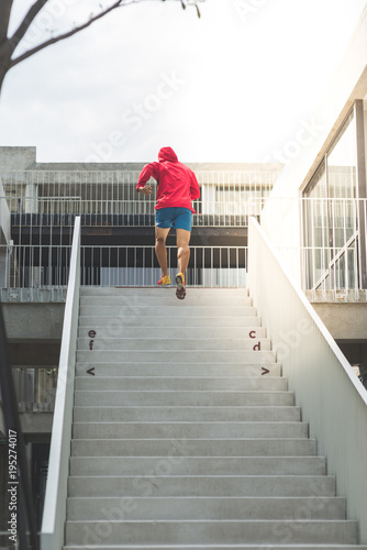 Back of sport man in red hood running up at steps, motion blur. © nuiiko
