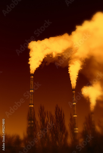 The thick smoke rises high from the industrial pipes. Pollution of the environment with waste products.