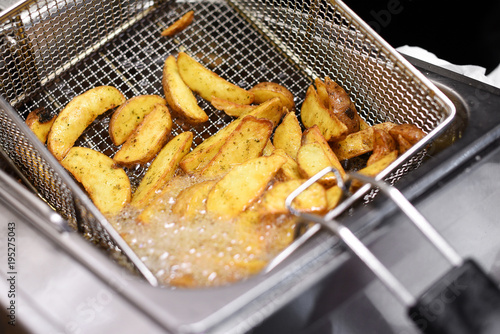 Spicy potato chips or wedges in a deep fryer