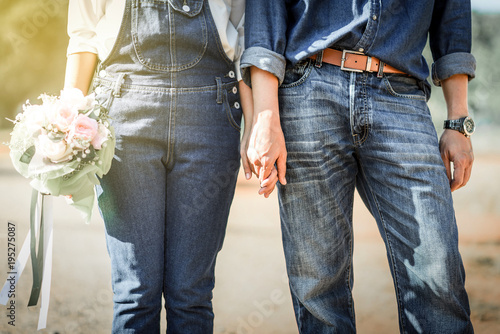 Young loving couple holding hands each other with wedding bouquet flowers , Bride and groom in vintage jeans standing together in soft light of sunset