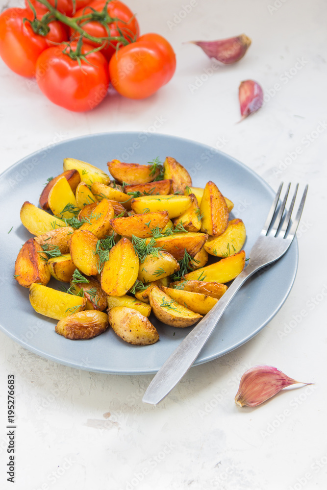 Fried potatoes in a plate. Baby potatoes, green, tomatoes and garlic on the table