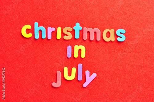 The words christmas in July in colorful letters on a red background