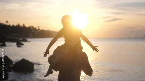 Son in eyeglasses sits on shoulders of his father raises hands imitating a flight at amazing sunset. slow motion. 3840x2160