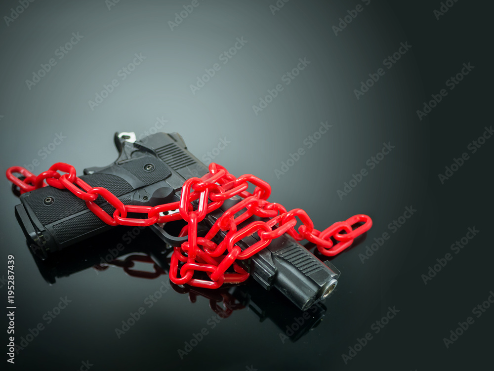 Naklejka premium reform gun control concept. red chain around handgun on black mirror with spotlight shine to the gun