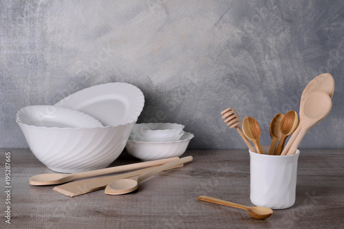  A set of wooden spoons in a white bowl on a gray background on a wooden table White dishware stacked on a wooden table against grey background on wooden table