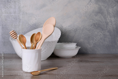  A set of wooden spoons in a white bowl on a gray background on a wooden table White dishware stacked on a wooden table against grey background on wooden table