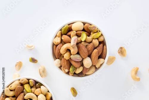 Fototapeta Naklejka Na Ścianę i Meble -  Healthy food and snack : mixed nuts in white ceramic bowl on white background from above, pistachios, almonds, hazelnuts and cashew.
