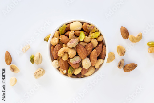 Fotografie Healthy food and snack : mixed nuts in white ceramic bowl on white background from above, pistachios, almonds, hazelnuts and cashew