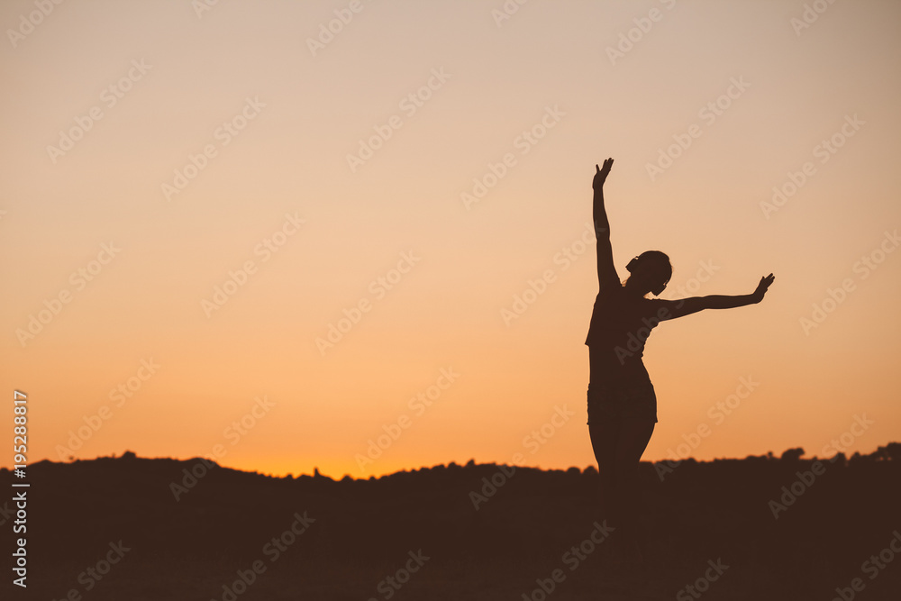 Silhouette of woman listening the music on sunset fiery sky