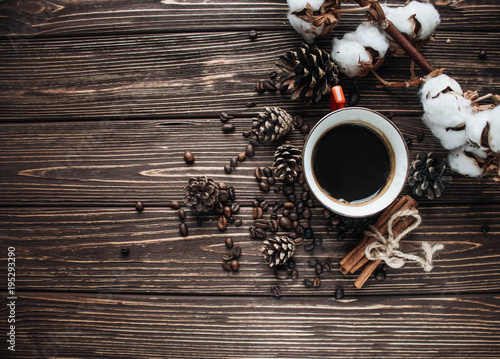 Close-up view of roasted coffee beans, cup of coffee, cotton flowers, cinnamon and pine cones