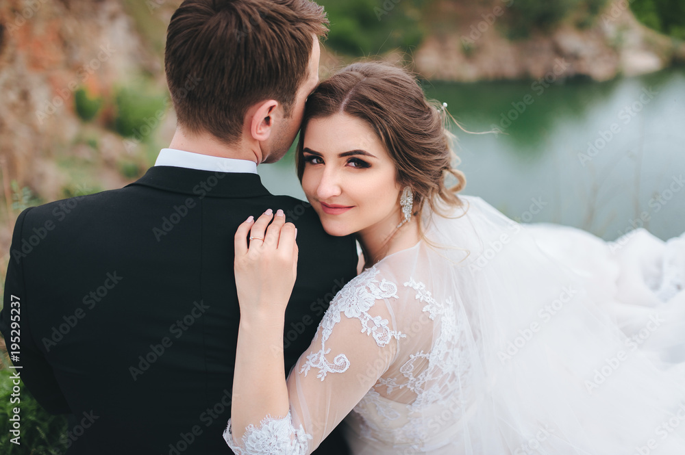 The bride and groom sit embracing against the rocks. The bride turned around and laid her head on her husband's shoulder. Close-up of the bride. A great wedding day. The bride and groom sit embracing against the rocks. The bride turned around and laid her head on her husband's shoulder. Close-up of the bride. A great wedding day.