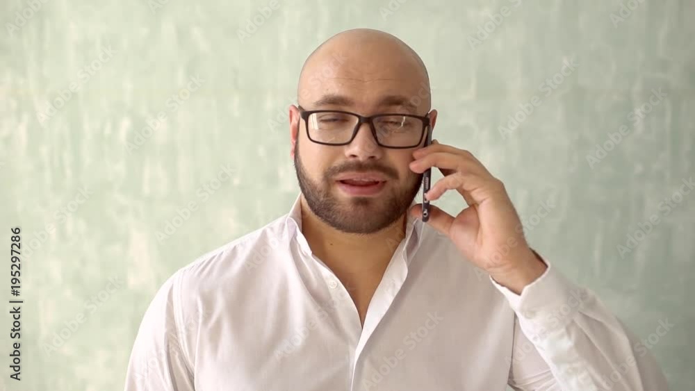 Close up of businessman bearded face talking on mobile phone. A Stylish man in a white shirt speaks on a mobile phone. Smart phone man calling on mobile phone. slow-motion. emotion and facial Close up of businessman bearded face talking on mobile phone. A Stylish man in a white shirt speaks on a mobile phone. Smart phone man calling on mobile phone. slow-motion. emotion and facial