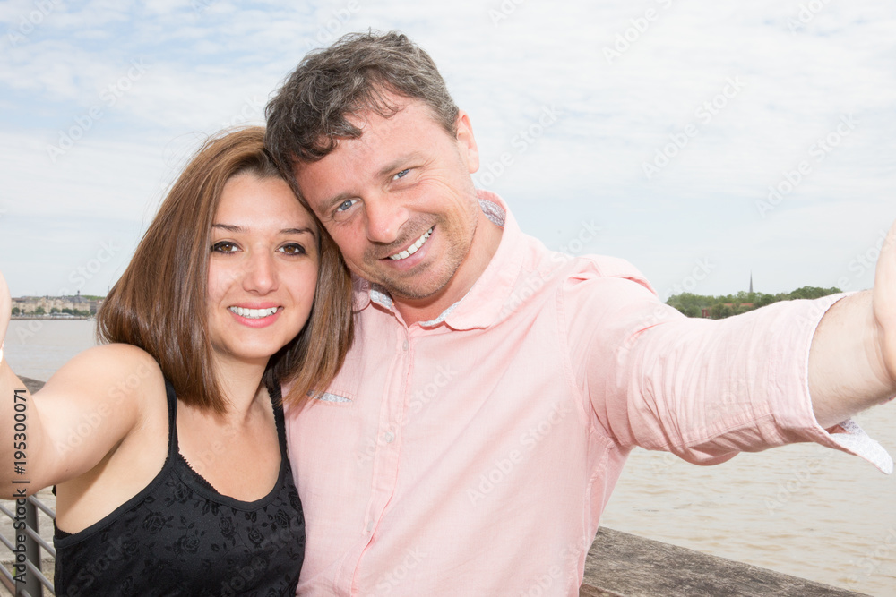 Happy young couple taking photos using mobile smart phone camera inear city river - Travel lovers making selfie portrait for social media network - obrazy, fototapety, plakaty 
