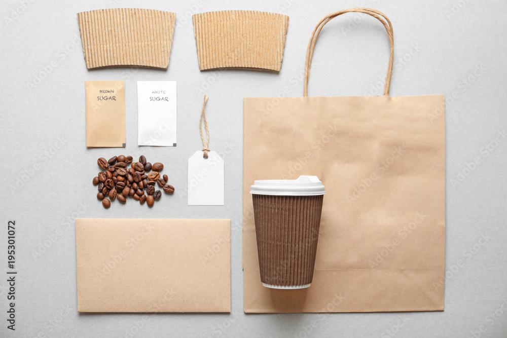 Composition with blank cup, paper bag and sugar packages as mockups for branding on grey background Composition with blank cup, paper bag and sugar packages as mockups for branding on grey background