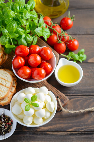 Italian food ingredients – mozzarella, tomatoes, basil and olive oil on rustic wooden table.