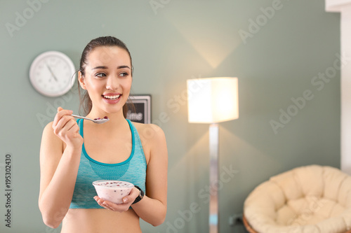 Sporty young woman eating yogurt with berries after fitness training at home