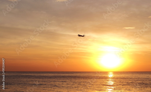 Silhouette of airplane flying over sea at the sunset