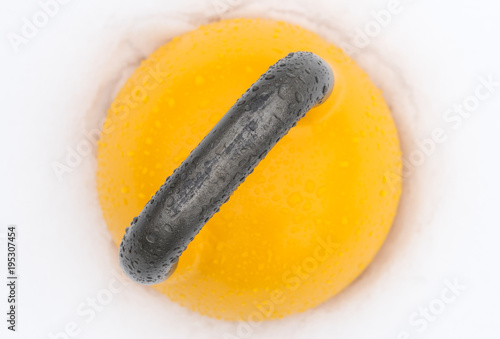 Top view of a yellow weight training kettlebell covered with water droplets outside in the snow. Yellow competition kettlebells weigh 16kg. photo