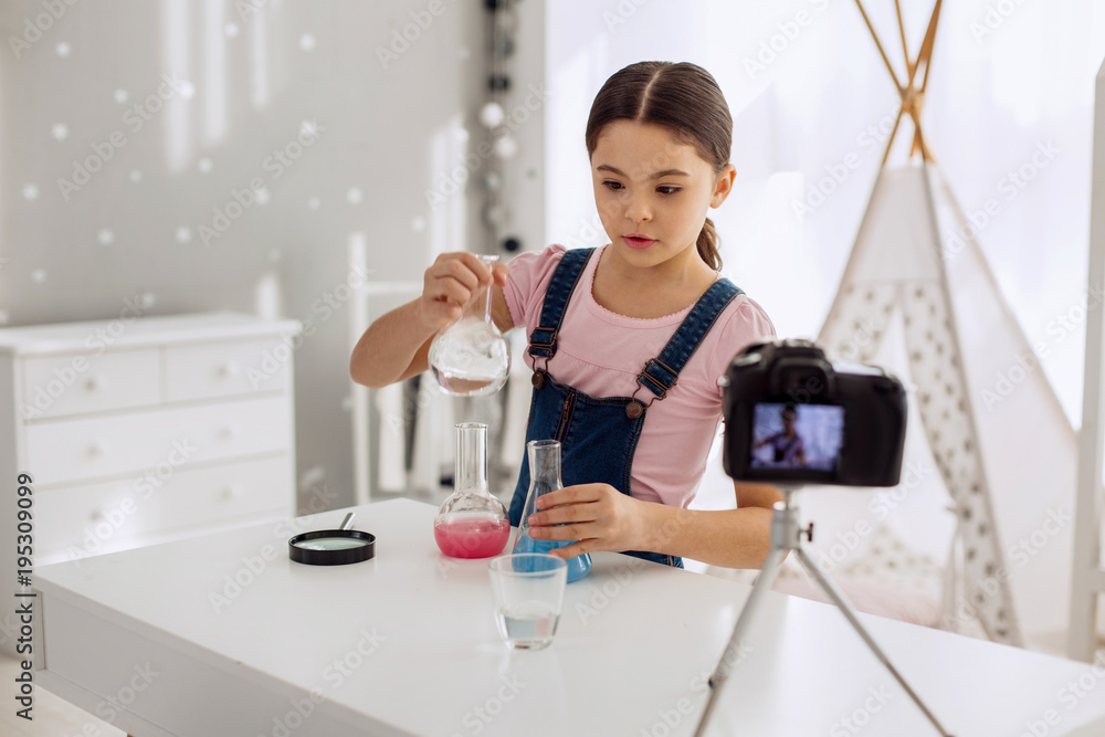 Young chemist. Pleasant pre-teen girl mixing the chemicals from different flasks and recording it on her camera, filming a video blog Young chemist. Pleasant pre-teen girl mixing the chemicals from different flasks and recording it on her camera, filming a video blog