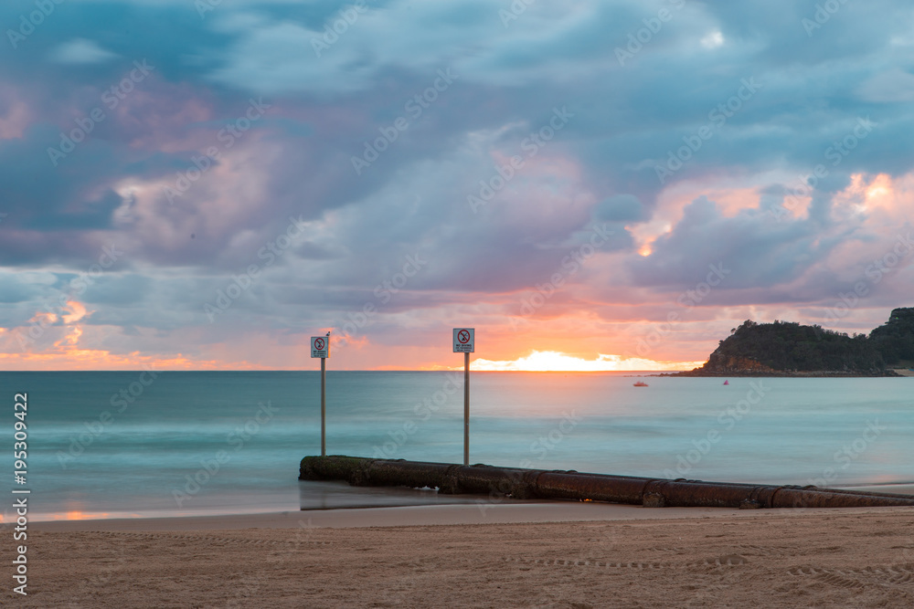 Sunrise glow above storm water pipe at Manly beach.