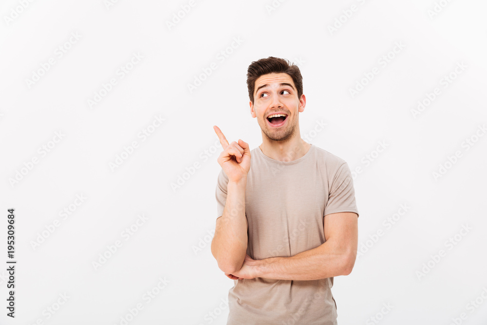 Positive brunette man 30s wearing beige t-shirt gesturing finger aside on copyspace, isolated over white background Positive brunette man 30s wearing beige t-shirt gesturing finger aside on copyspace, isolated over white background
