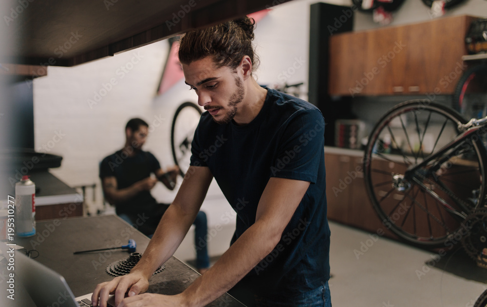 Mechanic working on laptop in bicycle workshop Mechanic working on laptop in bicycle workshop