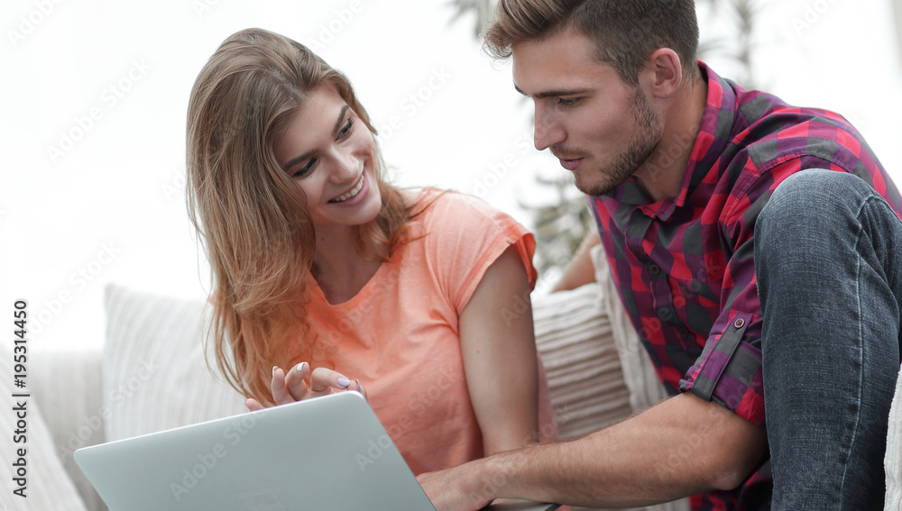 young couple is using a laptop and smiling while sitting on sofa at home young couple is using a laptop and smiling while sitting on sofa at home