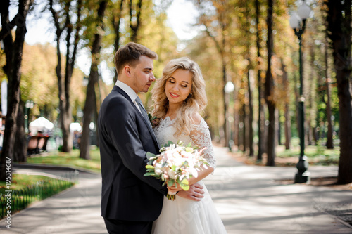 Portrait of a bridegroom embracing a blonde bride in the park