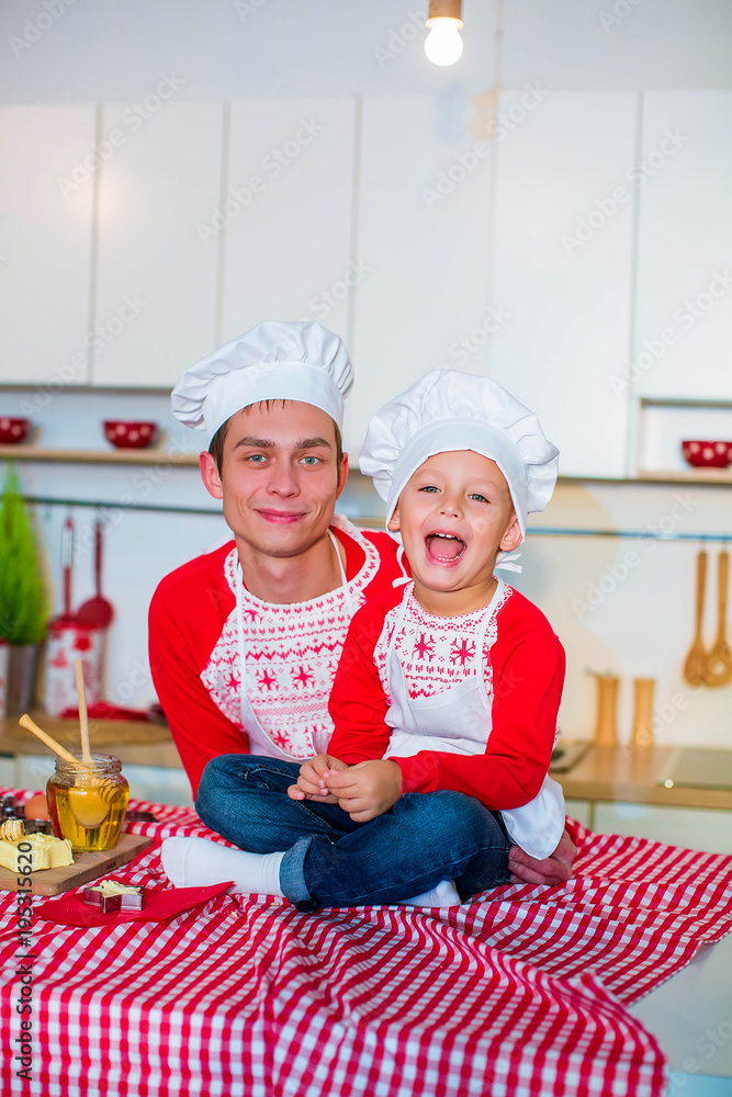 Preparation of a sweet dessert. Father with happy son in aprons and hat in an interior kitchen. Preparation of a sweet dessert. Father with happy son in aprons and hat in an interior kitchen.
