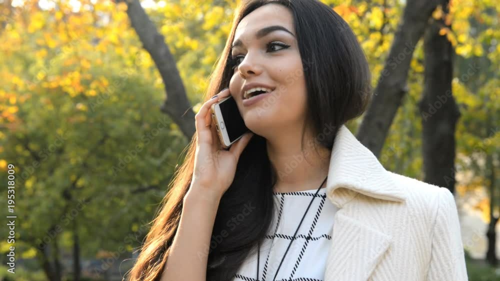 Young beautiful brunette is standing near a tree in the street and talking on the phone. Young beautiful brunette is standing near a tree in the street and talking on the phone.