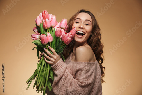 Happy smiling girl with long brown hair receiving bouquet of pink tulips on women's day, isolated over beige background #195324271