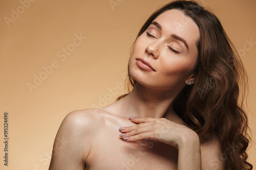 Photo of nude attractive female 20s with natural makeup posing on camera with closed eyes, isolated over beige background