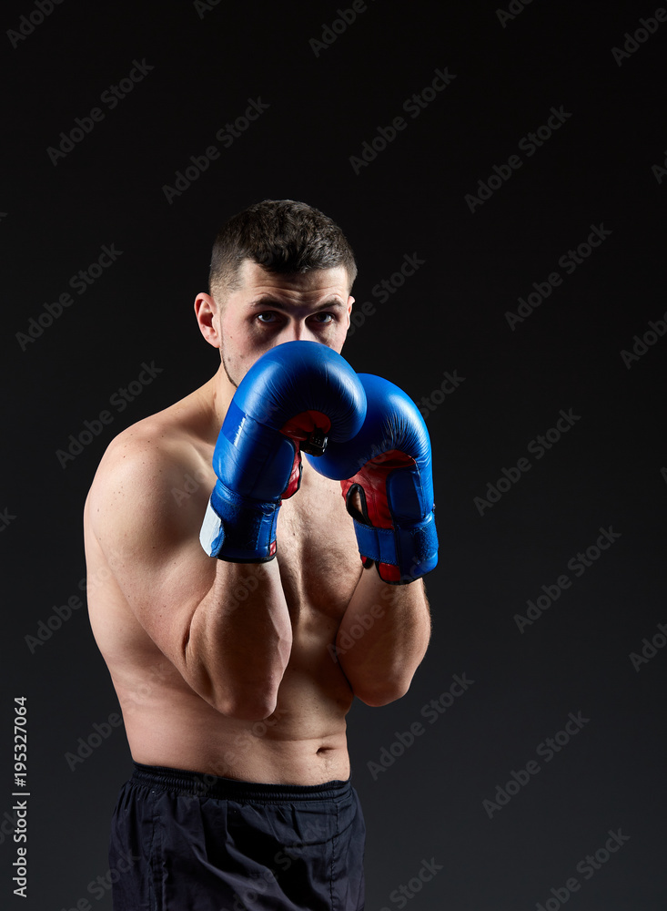 Low key studio portrait of handsome muscular fighter practicing boxing on dark blurred background