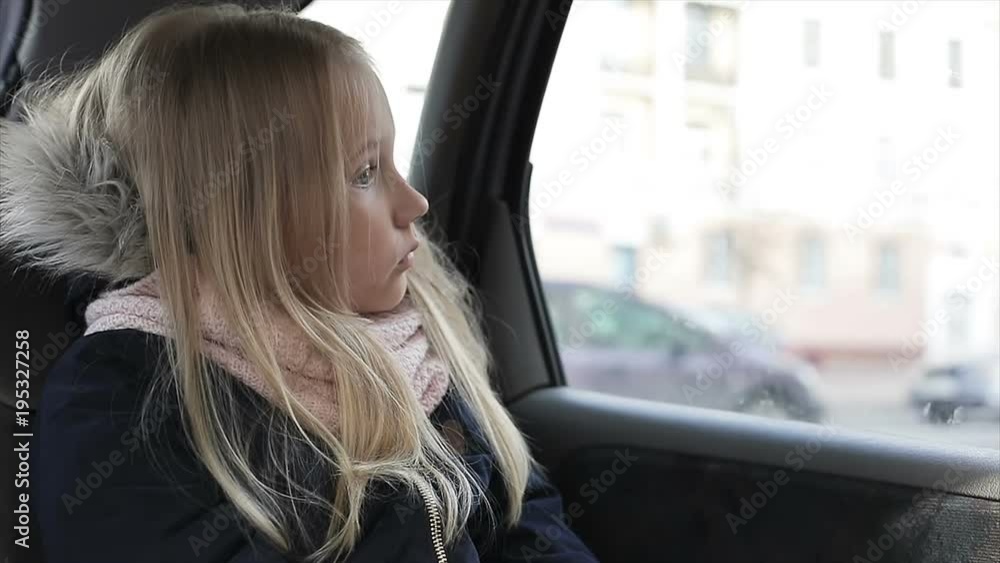 Sad child looking to the car window. Little blonde girl on a back seats in car. Sad child looking to the car window. Little blonde girl on a back seats in car.