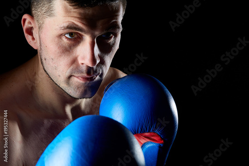 Close up low key portrait of an aggressive muscular fighter, showing his fist isolated on dark background.