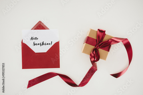 top view of red envelope with hello sunshine lettering on paper and gift box isolated on white