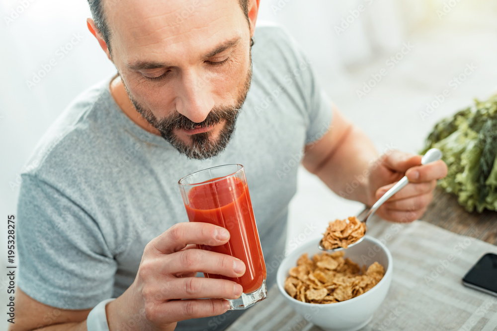 Fresh juice. Handsome calm pleasant man sitting by the table eating and drinking tomato juice. Fresh juice. Handsome calm pleasant man sitting by the table eating and drinking tomato juice.