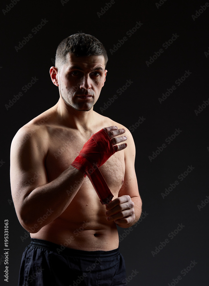Low key studio portrait of handsome muscular fighter preparing for boxing on dark blurred background