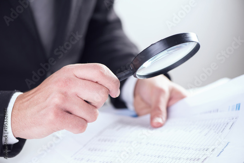 Businessman checking a tablet with magnifying glass