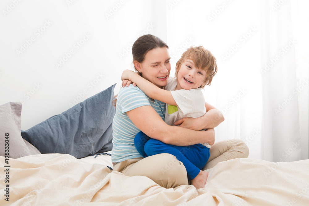 little son is hugging and kissing her  mom and  relaxing and playing in the bed at the weekend together, lazy morning. Mother's day.