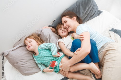 mother with her little children, son and daughter, relaxing and playing in the bed at the weekend together, lazy morning. 
