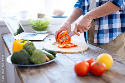 Weight loss. Close up of young male hands slicing red bell pepper for cooking salad and holding knife