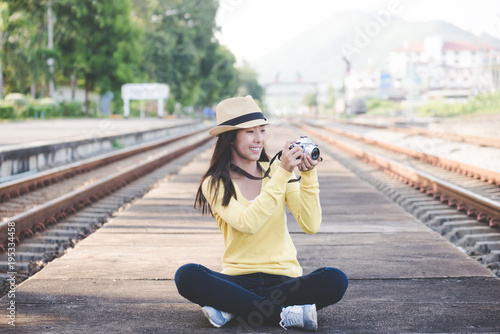 Traveler and tourist asian women wearing backpack holding camera and sit near station the train. Travel Concept.