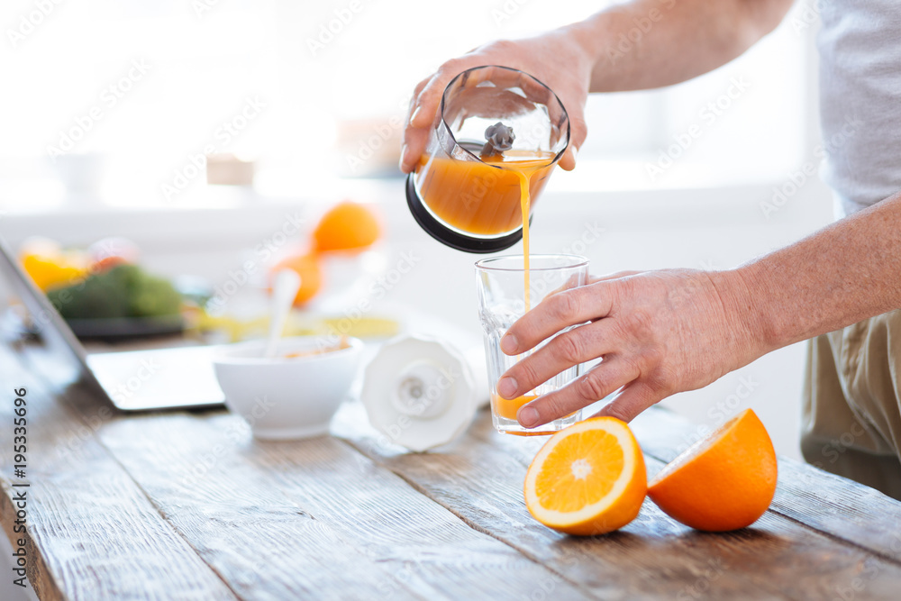 Orange scent. Close up of male hands holding transparent clean glass while spilling orange juice and consuming vitamins Orange scent. Close up of male hands holding transparent clean glass while spilling orange juice and consuming vitamins