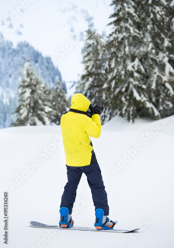Young man with photo camera on snowboard